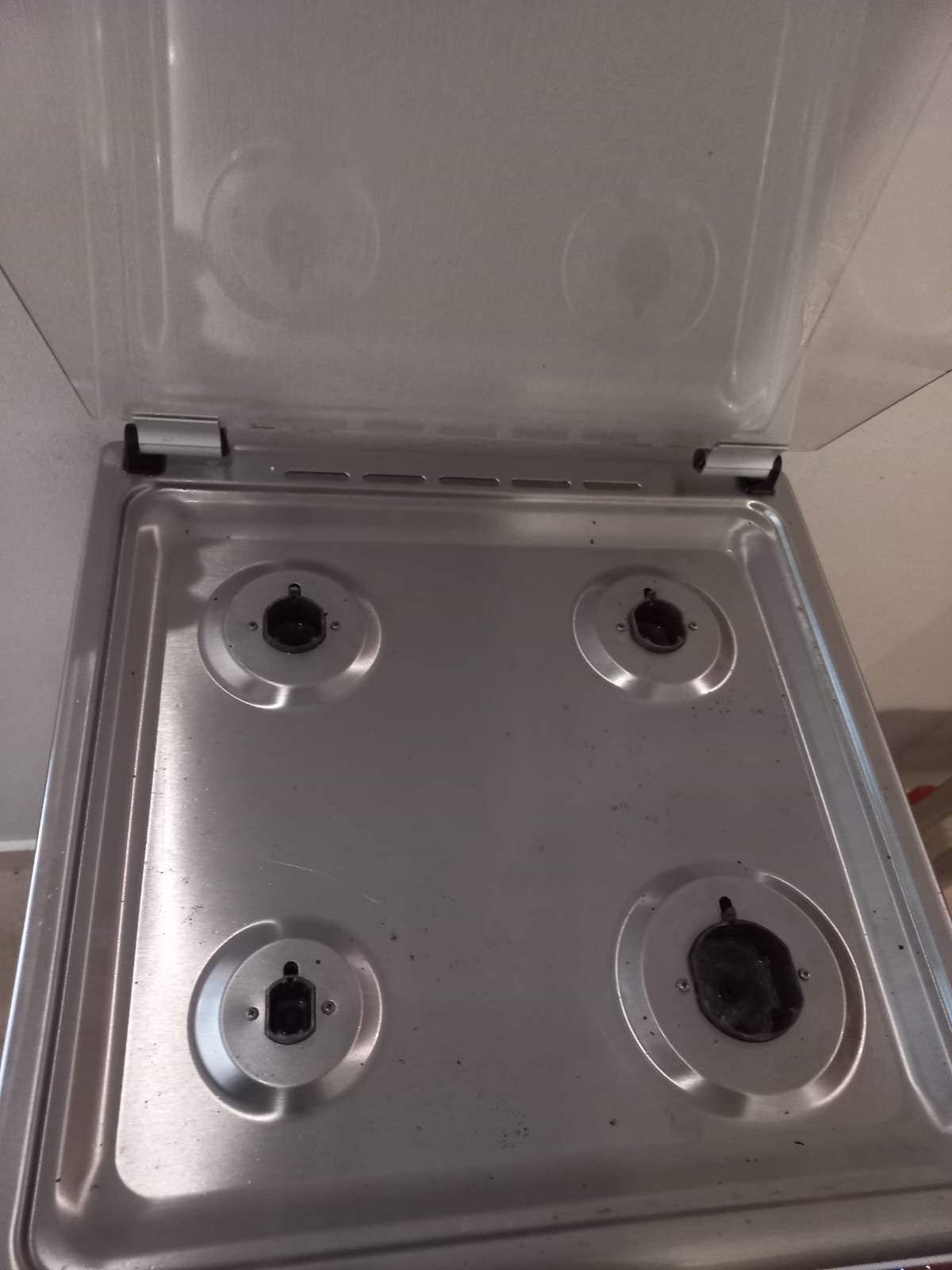 Stainless steel gas stovetop with four burners and a raised glass lid.