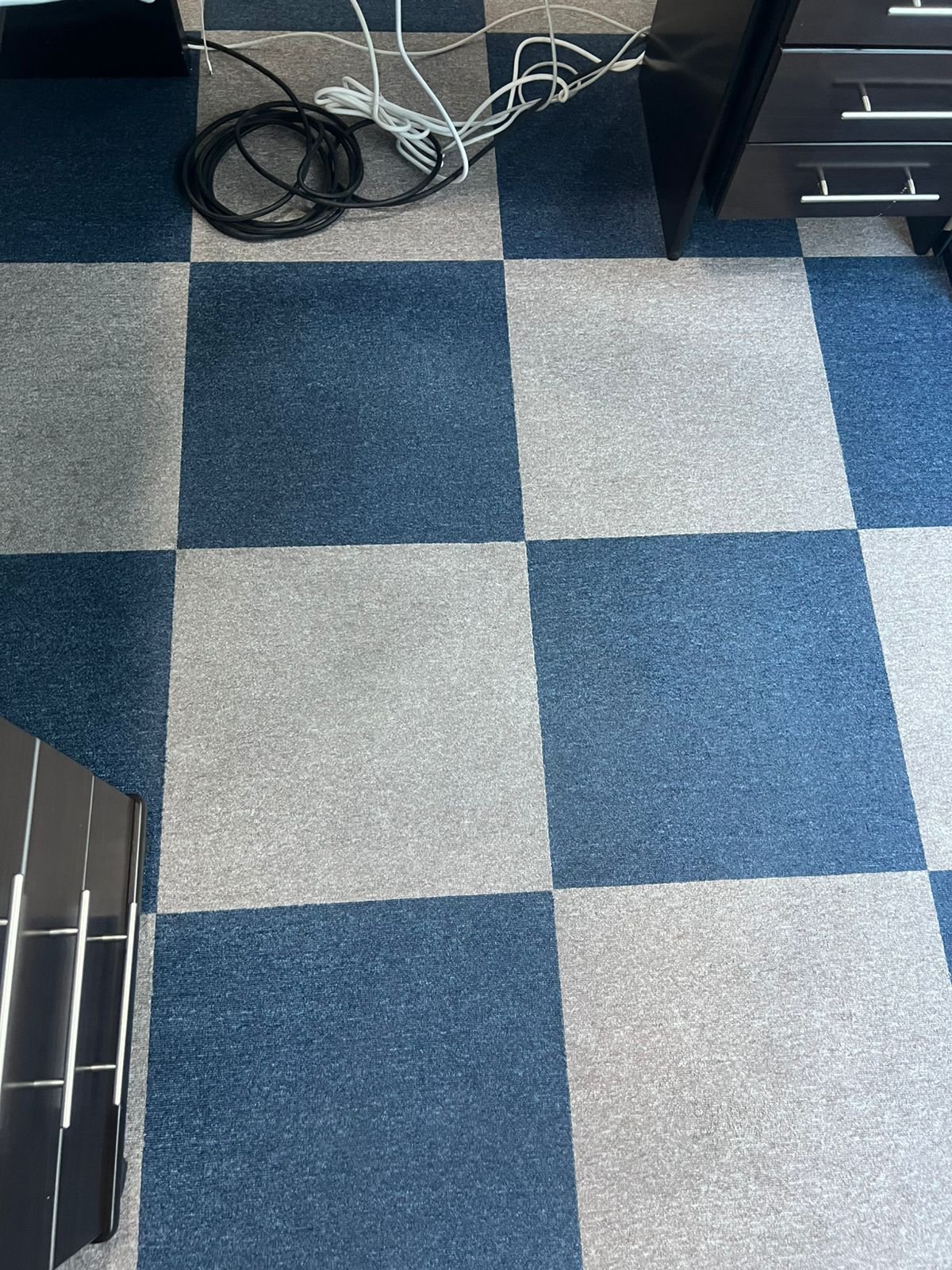 Office carpet with blue and grey squares, with cables and a filing cabinet.