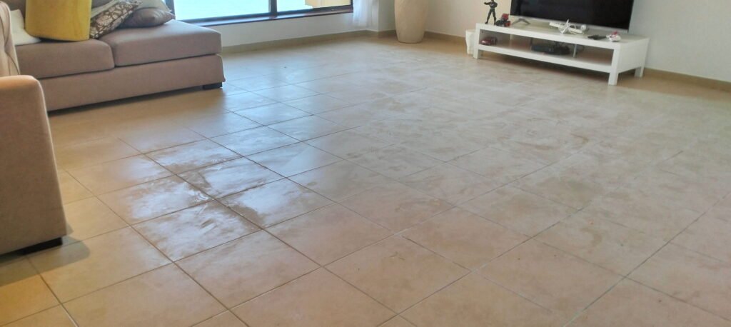 Tiled living room floor with a wet patch near a beige sofa.