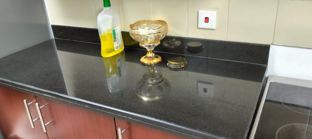 Dark granite kitchen countertop with dish soap, decorative bowl, and cabinets.